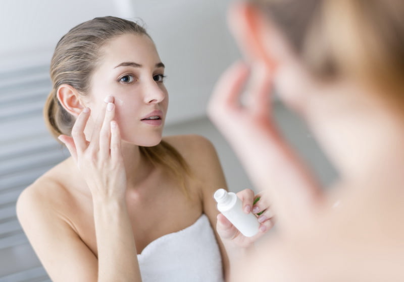 young woman applying skin cream to her face