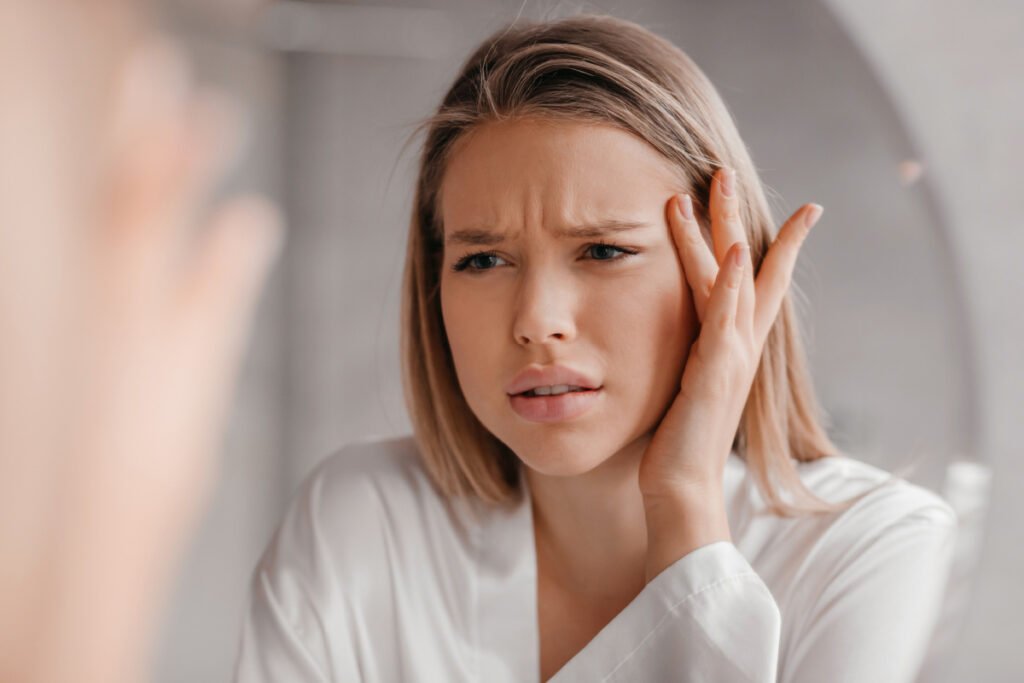 Young woman frowning at forehead winkles and furrows in mirror